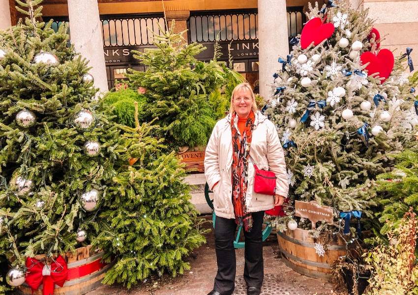 Lots of Christmas trees and a lady standing in the middle with a red bag