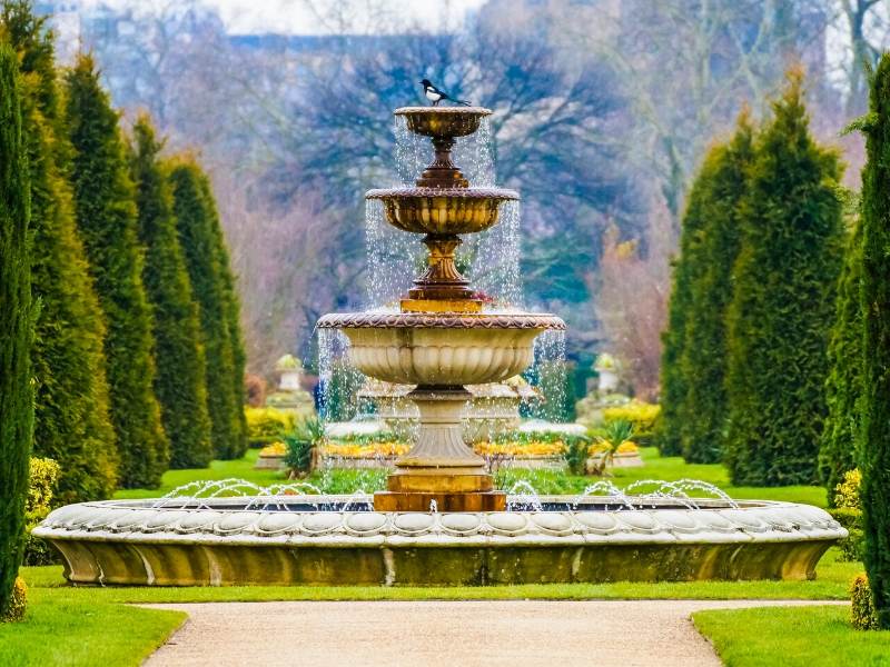 A large fountain surrounded by trees in manicured gardens