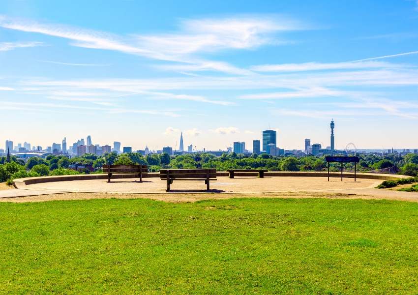 A view of London from Primrose Hill with blue skies and empty benches