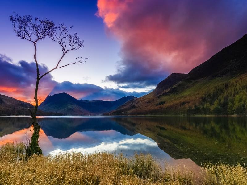 A picture of the Lake District showing a lake and a pink sky reflected in it this is one of the top places to visit in North West England