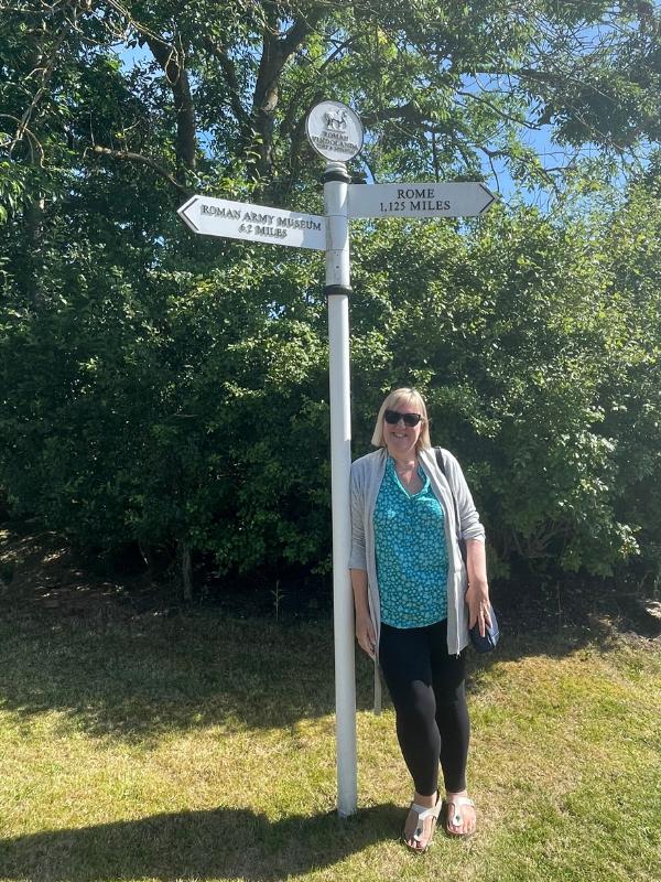 Lady standing near a sign for the Roman Army Museum in Northumberland.