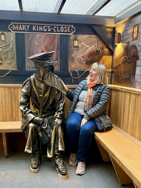 Tracy sitting beside the bronze plague doctor statue at The Real Mary King's Close in Edinburgh