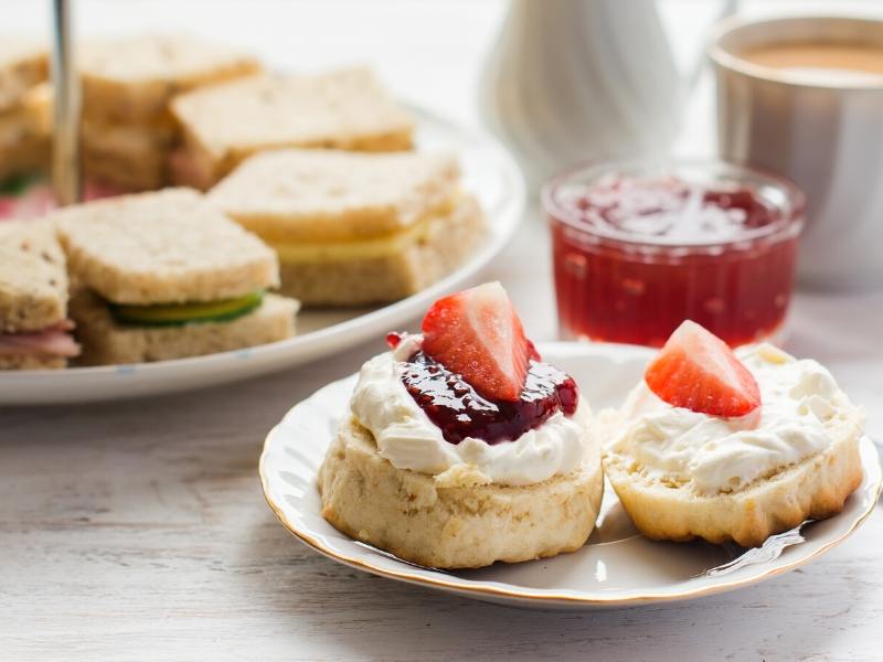 A selection of foods at an afternoon tea including scones with jam and cream.