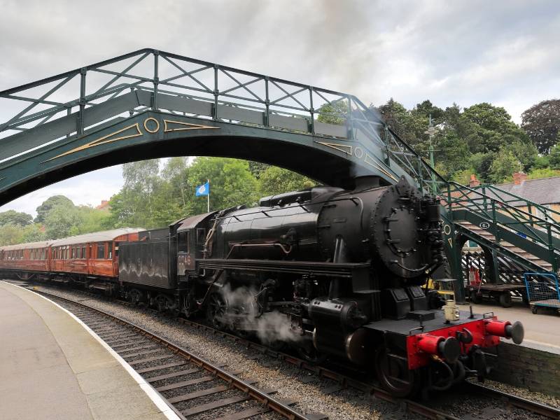 A steam train pulling up underneath a bridge at Pickering train station in England