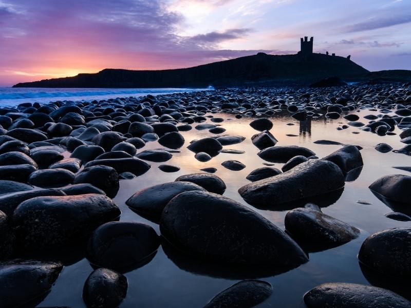 A silhouette of Dunstanburgh Castle at sunset