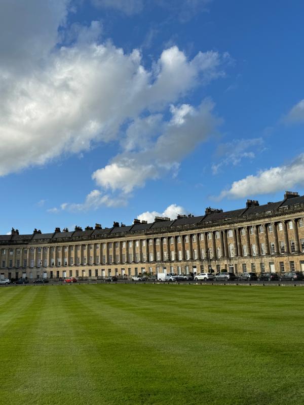 a large building with a lawn and cars parked in front of it with Royal Crescent in the background