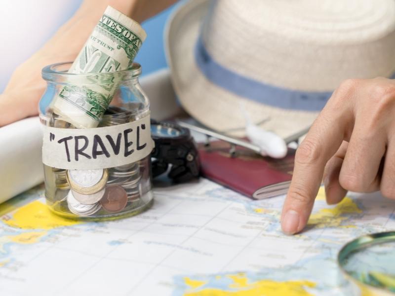 UK trip planner pointing at a map with cash in a jar labelled travel