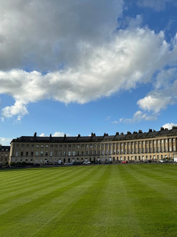 a large lawn with Royal Crescent and clouds in the sky