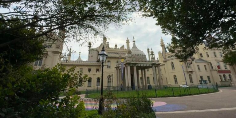 The Royal Pavilion in Brighton framed by trees in the Pavilion Gardens, with a lamp post and rainbow painted path