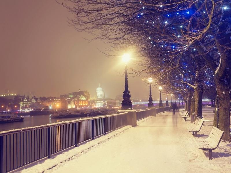 Night in London with snow and twinkling lights in the trees.