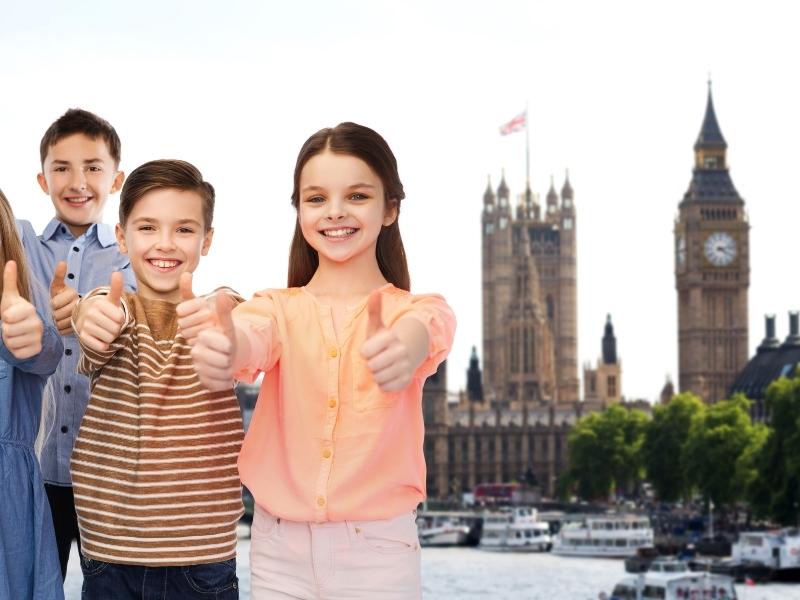 Some kids holding their thumbs up in front of Big Ben in London.