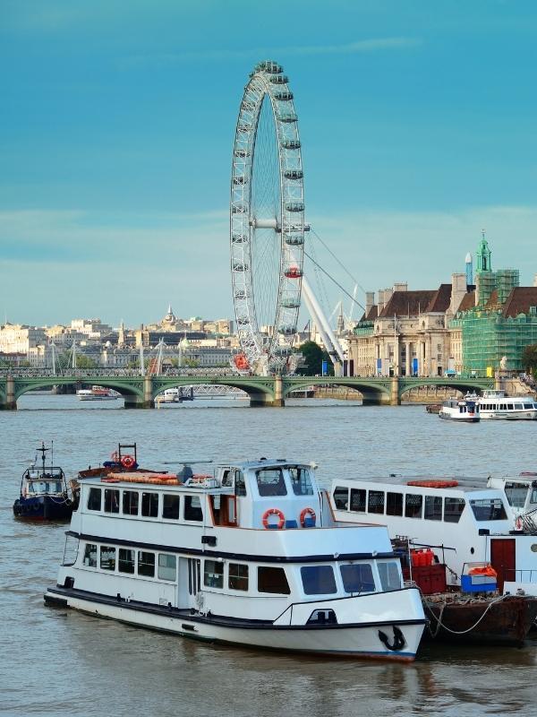 Boats on the River Thames in London with the London Eye behind them.