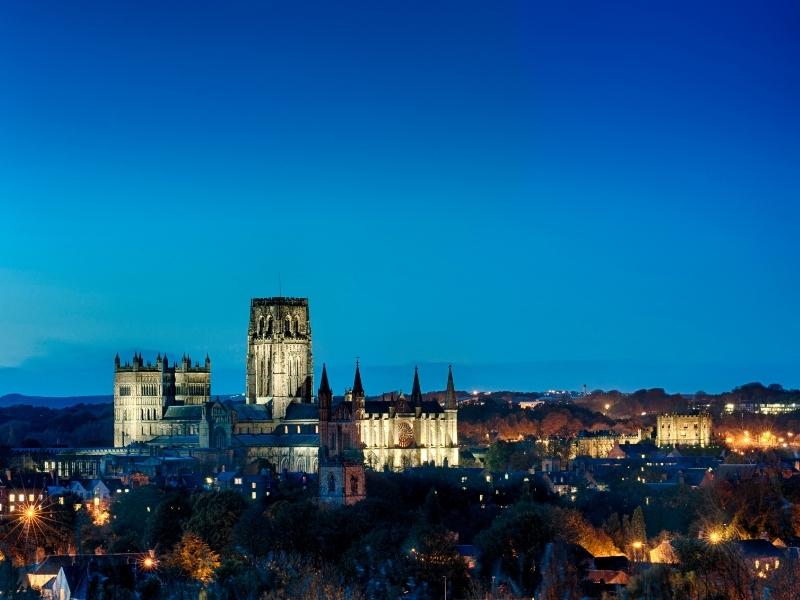 A photo of Durham cathedral lit up at night with the city lights below.