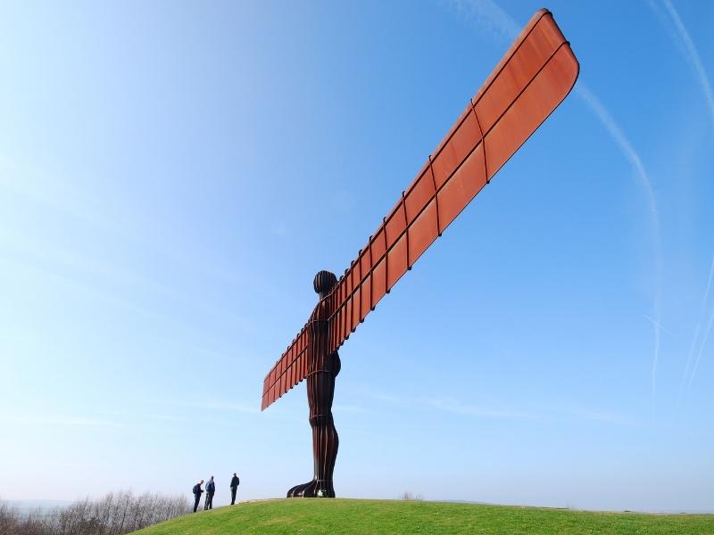 A photo of the Angel of the North Statue with 3 people standing beneath.