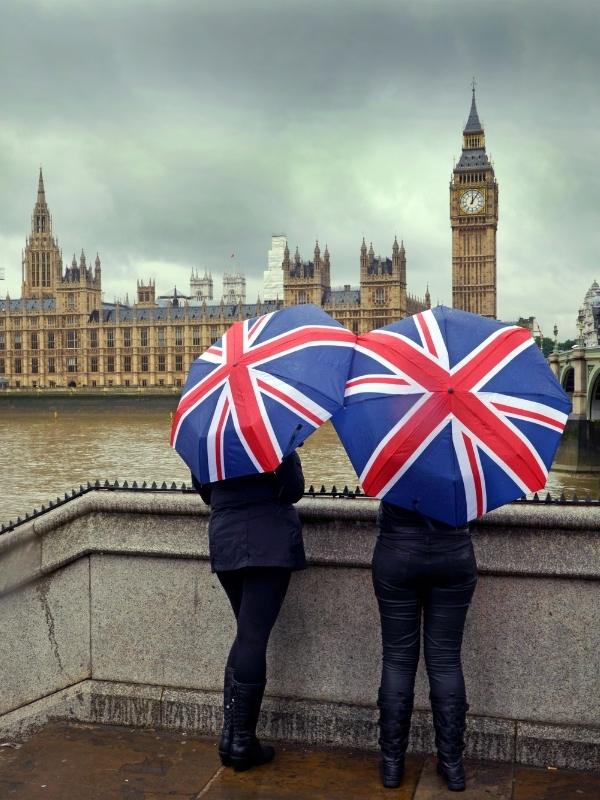 Houses of Parliament in London with two people holding Union Jack umbrellas.