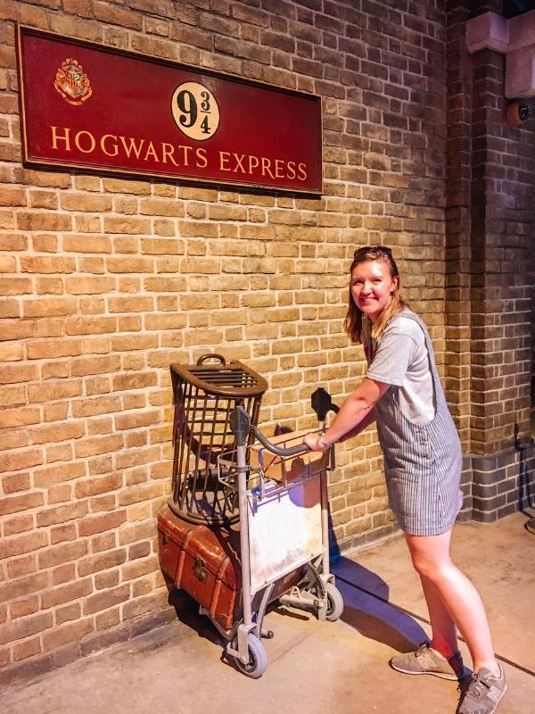 A girl pushing a baggage trolley into a wall beneath a sign for the Hogwarts express.