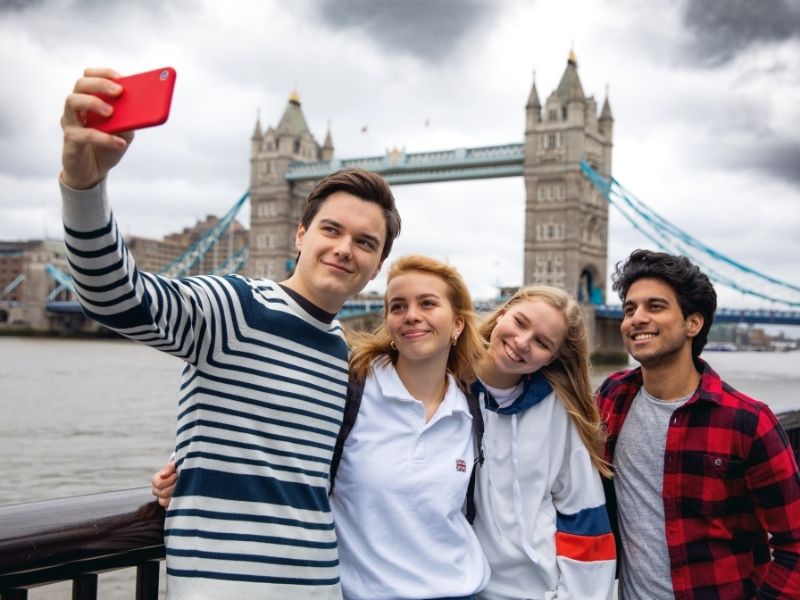 Teenagers posing for a selfie in front of Tower Bridge.