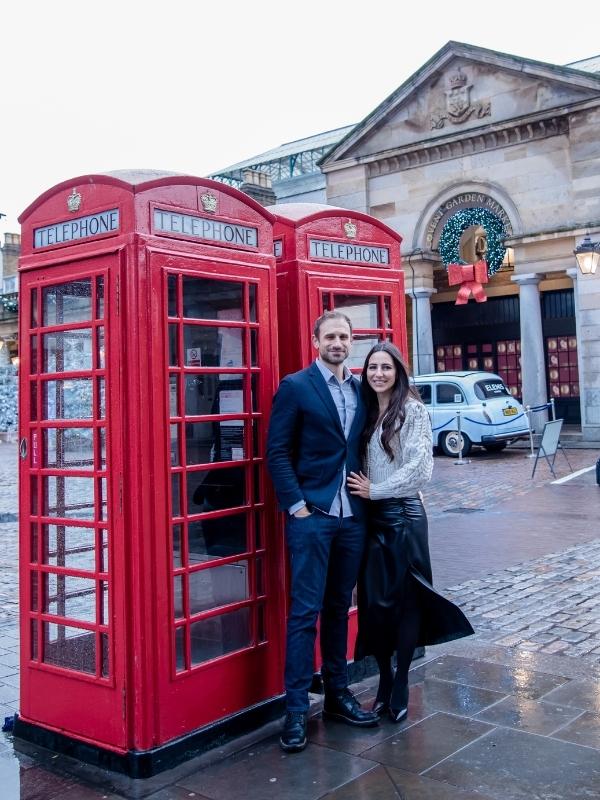 A couple standing next to 2 London red phone booths at Christmas.