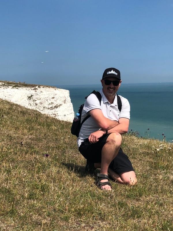 Man keeling with the White cliffs of Dover behind him.