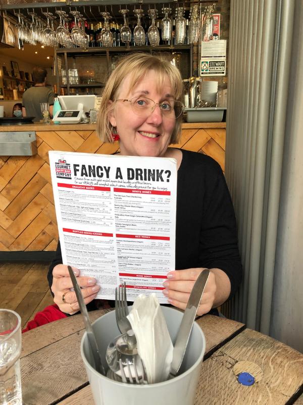 A lady holding a menu which says "Fancy a drink" at Makar's Mash Bar in Edi