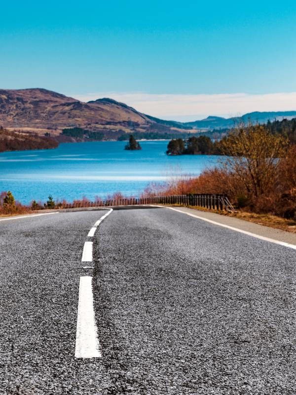 UK road trip planner pic of a Scottish road leading to a loch.