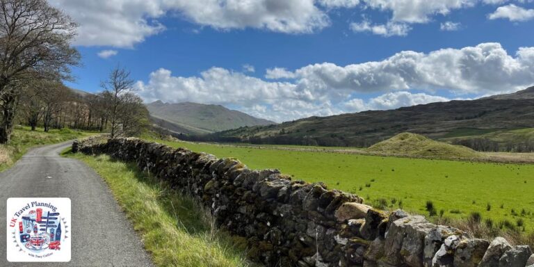 Road with a green field and a stone wall next to it.
