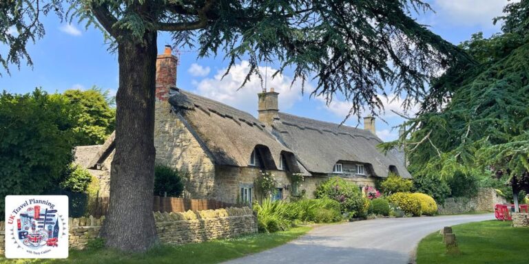 A traditional thatched stone cottage surrounded by summer gardens in a Cotswolds village on a sunny day