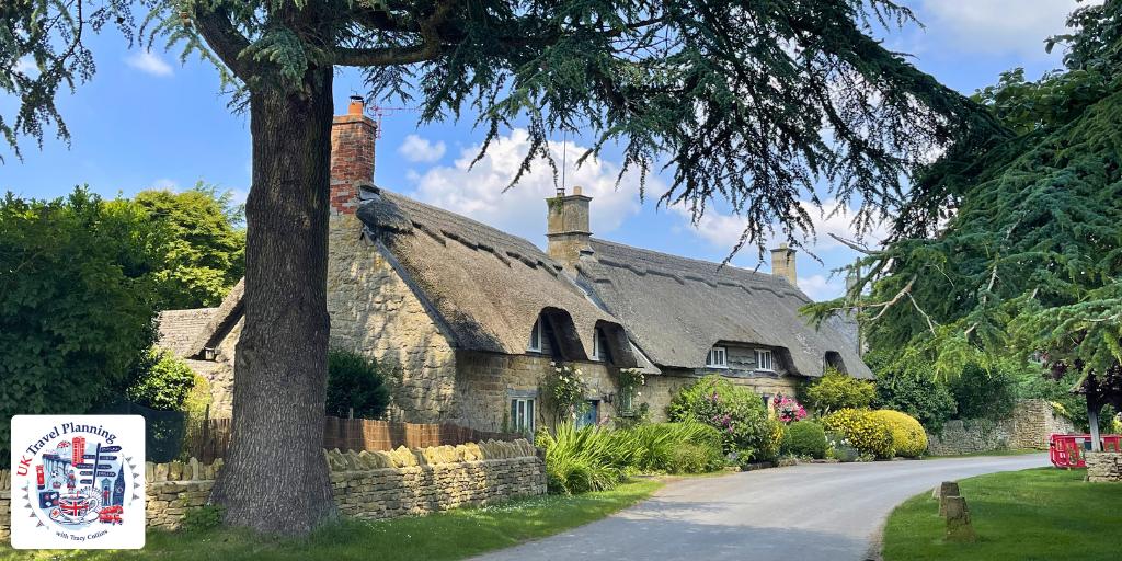 A traditional thatched stone cottage surrounded by summer gardens in a Cotswolds village on a sunny day