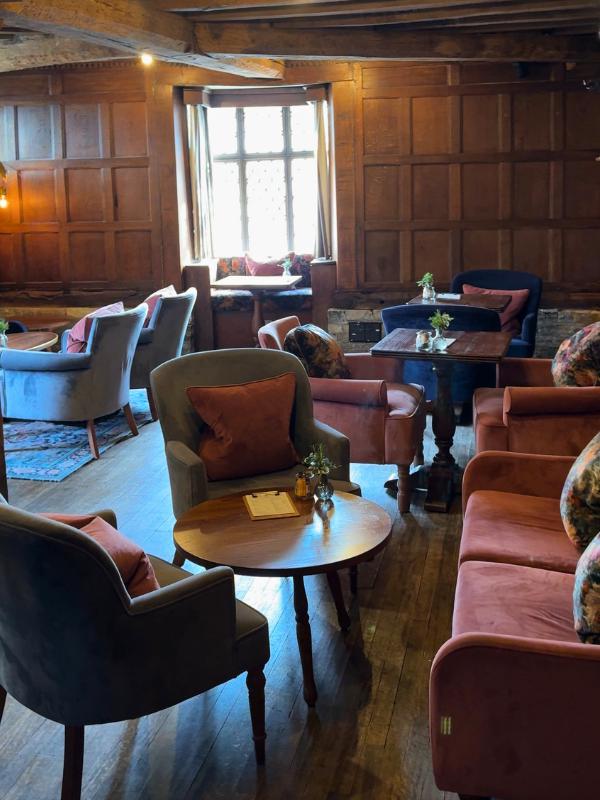 Sala de estar del hotel con carácter, con vigas de madera originales a la vista, paredes con paneles de roble, ventanas emplomadas, alfombra persa y sofá de terciopelo azul con cojines de terracota.