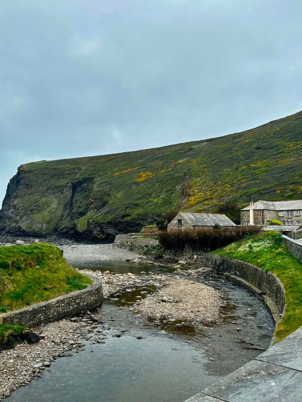The winding river and stone cottages of Boscastle harbour below a green hillside
