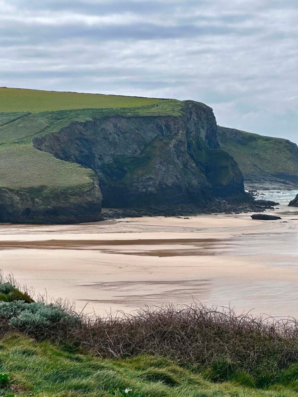 A sandy beach cove framed by rugged green cliffs on the Cornwall coast path