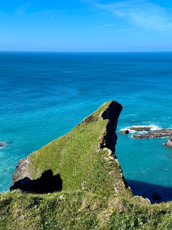 A grassy headland jutting into bright turquoise sea on the Cornwall coast