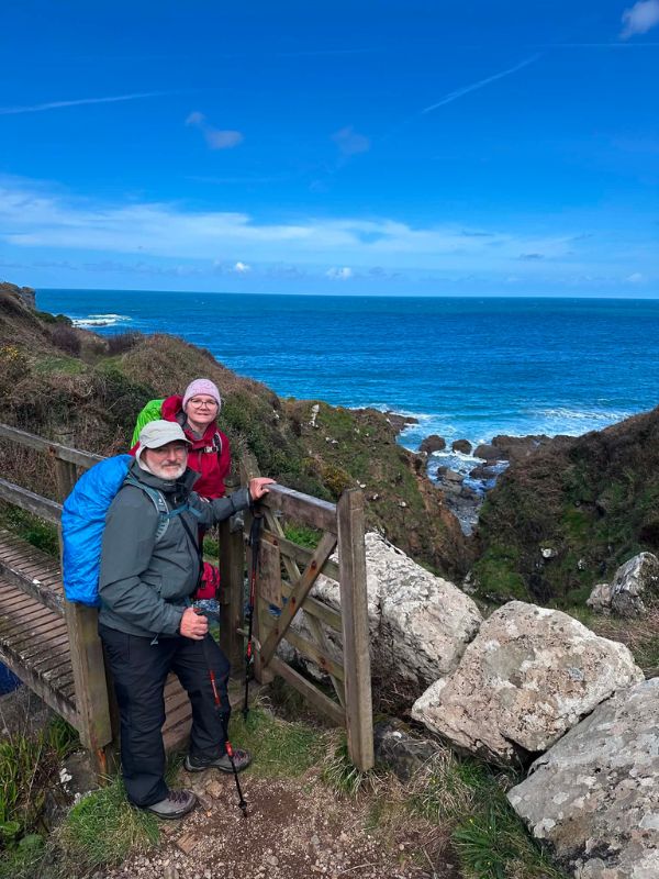 Katherine and Glen at a wooden gate on the coast path with the sea behind