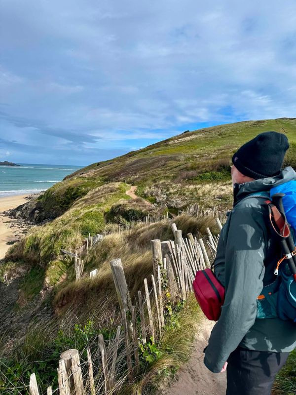 A walker looking down a dune path towards a sandy Cornish beach