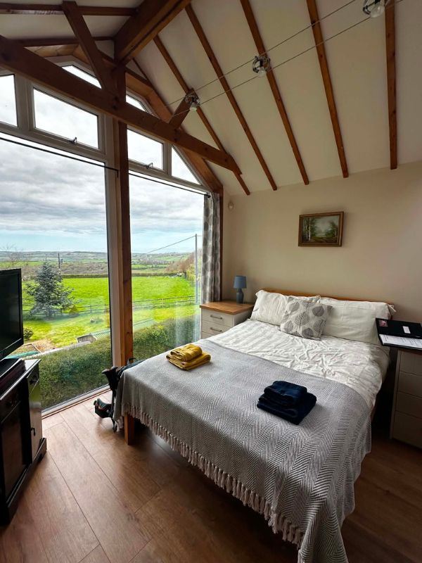 A bed and breakfast room with a full-height window looking out over green countryside