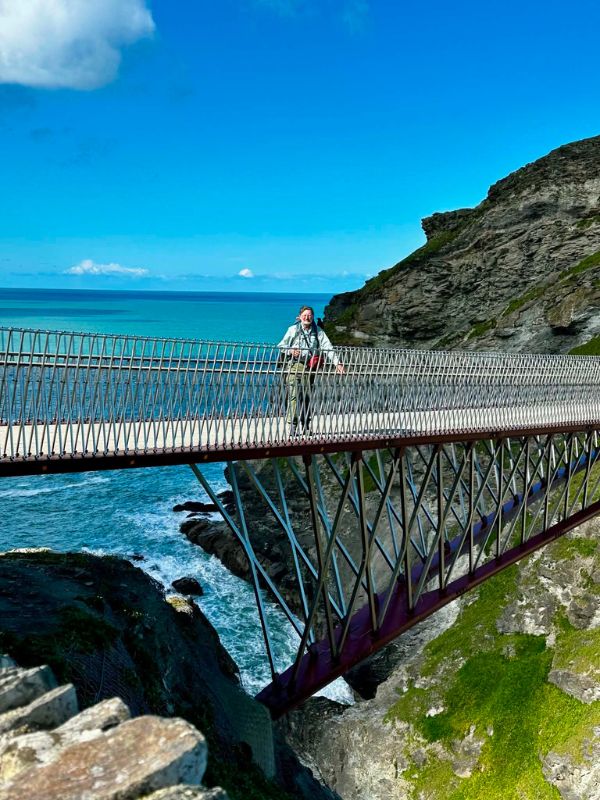 A walker crossing the footbridge to Tintagel Castle above the turquoise sea