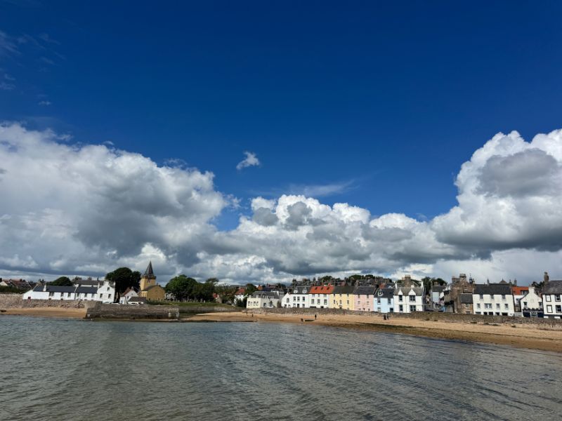 A sandy beach at Anstruther with whitewashed and pastel houses and a church spire along the shore