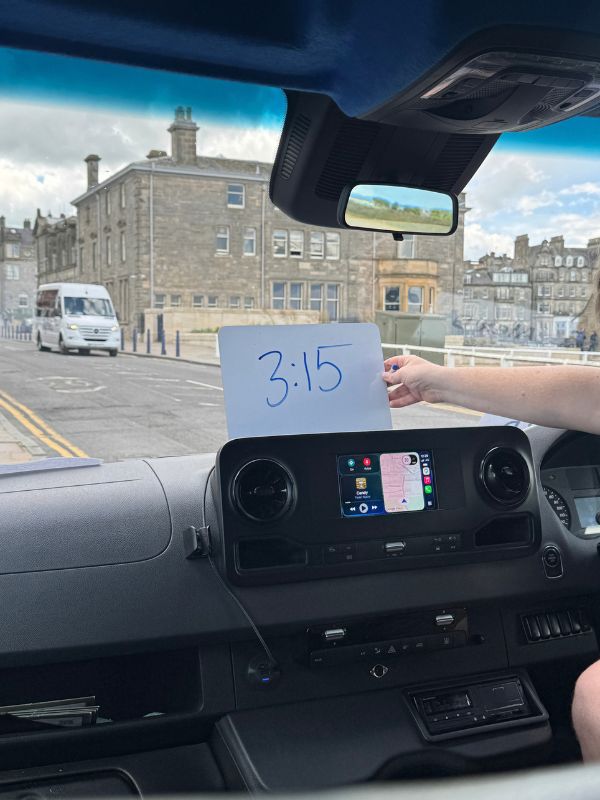 The Rabbie's driver guide holding up a card showing the 3:15 meeting time from the front of the minibus