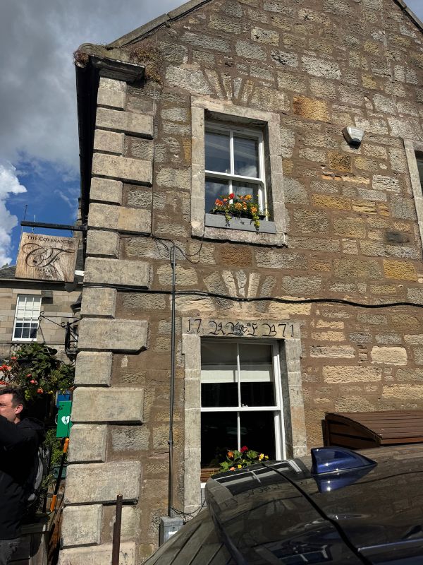 The Covenanter in Falkland, a stone building with a carved 1771 date stone above the window and flowers on the sills