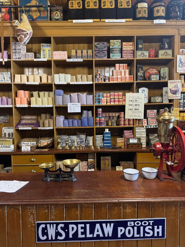 Brass scales and a red coffee grinder on the Co-op grocery counter at Beamish Museum, with shelves of packaged goods behind