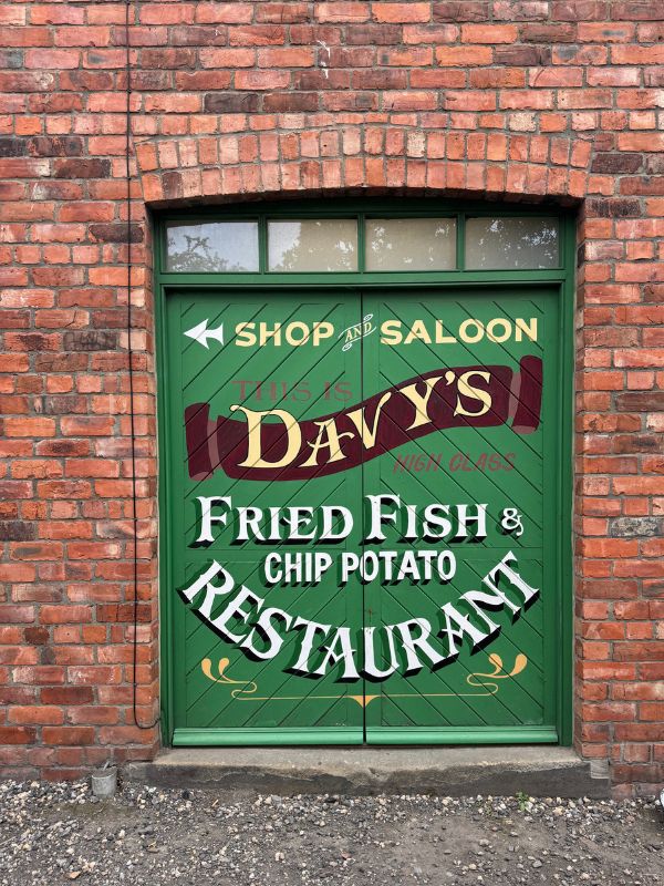 Green painted doors signed Davy's Fried Fish and Chip Potato Restaurant in a red brick wall at Beamish Museum
