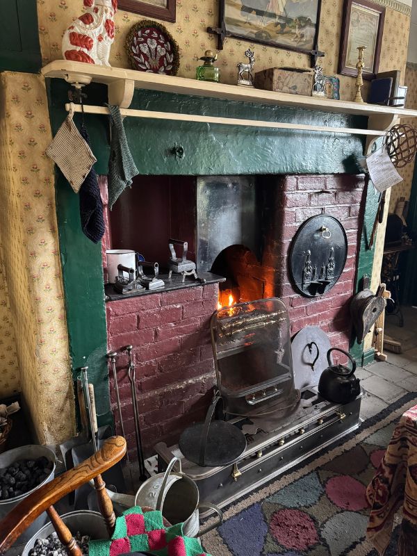 Kitchen range with a coal fire burning, a black kettle and a rag rug in a period home at Beamish Museum