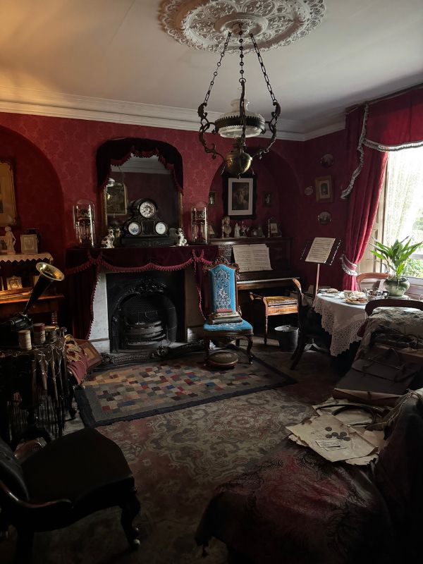 Parlour at Beamish Museum with red wallpaper, a piano, a gramophone and a cast iron fireplace