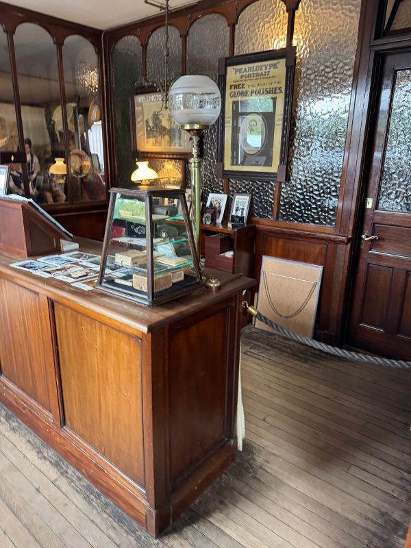 Wooden shop counter with a glass display case and brass lamp in a period shop at Beamish Museum