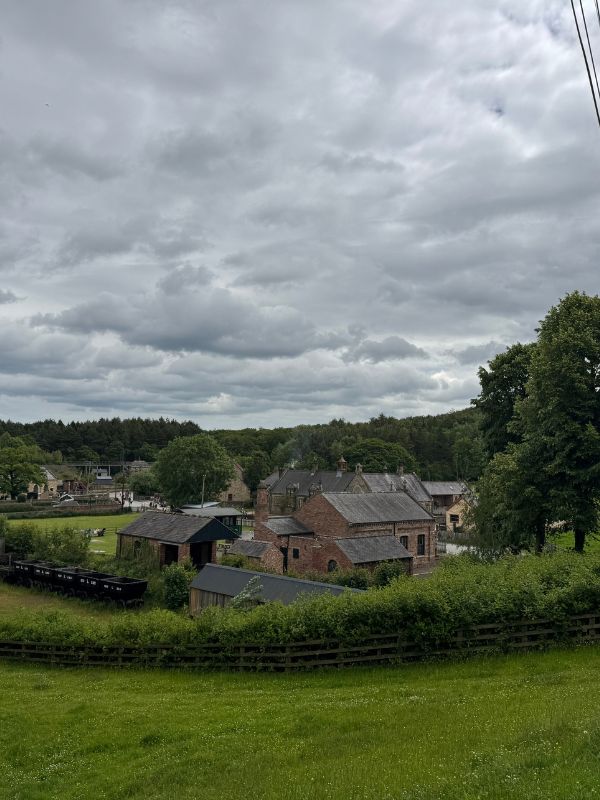 View over red brick buildings, coal wagons and woodland at Beamish Museum under a cloudy sky